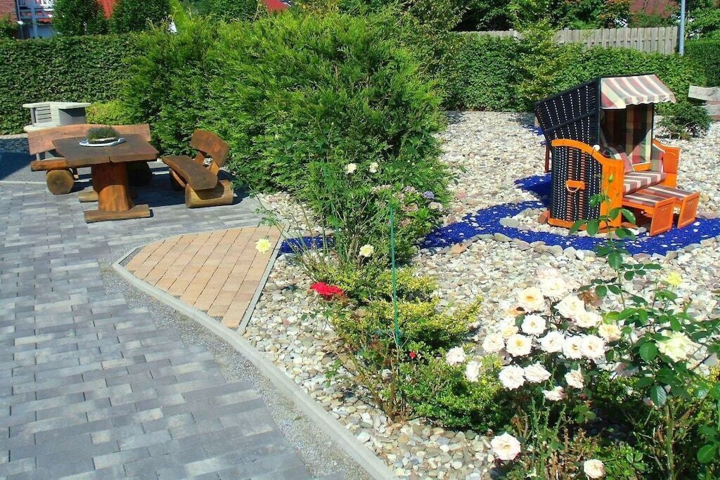 A garden with a wooden table and chairs, a small structure with a striped awning, and a variety of plants and flowers.