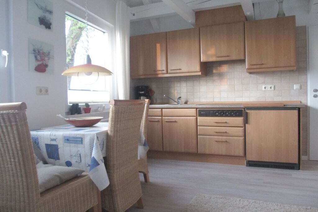 Une cuisine avec des meubles en bois, un coin repas avec des chaises en osier et une fenêtre qui laisse entrer la lumière naturelle.