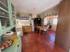 A kitchen with a tiled floor, wooden cabinets, a table with baskets, and a window with bars. - Country house near the city, peace and quiet, nature, a pool, and a large garden. (Bucelas)
