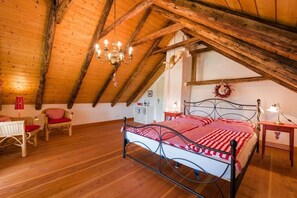 A bedroom with a sloped ceiling, a bed with a metal frame, two chairs with red cushions, a chandelier, and a small table with a lamp. - Holiday home with 2 bedrooms (Forlitz-Blaukirchen)