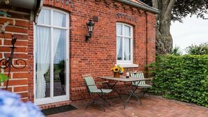 Un bâtiment en briques doté d’un patio comprenant une table et des chaises, une fenêtre avec des rideaux et un luminaire fixé au mur.
