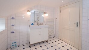 Une salle de bain avec un sol carrelé de carreaux blancs, un lavabo blanc, un miroir et une porte.