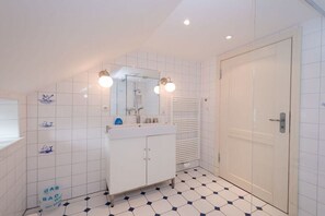 Un baño con piso de baldosas blancas, un lavamanos blanco, un espejo y una puerta.