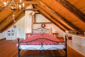 Un dormitorio con techo inclinado, cama con estructura metálica, mesitas de noche, estantería y candelabro.
