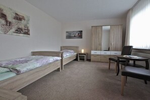 Une chambre avec deux lits simples, un bureau, une chaise, une armoire et une petite table de chevet.