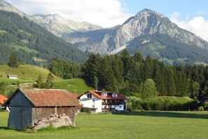 A rural landscape with a mountain backdrop, a wooden barn, and a white house with a red roof. - Holiday apartment with 1 bedroom (Sonthofen)