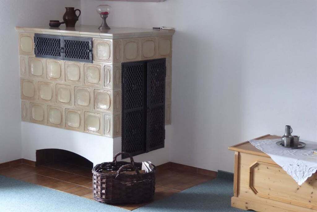 A room with a tiled floor, a white cabinet with a patterned top, a wooden table with a lace tablecloth, and a wicker basket.