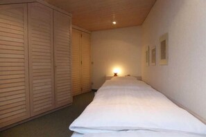 Een smalle gang met een bed aan het einde, een kledingkast en een wandlamp.