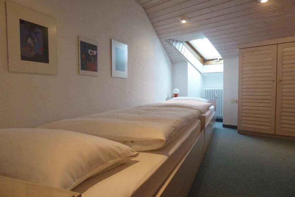 A room with three beds aligned against the wall, a skylight, and a door leading to another room.