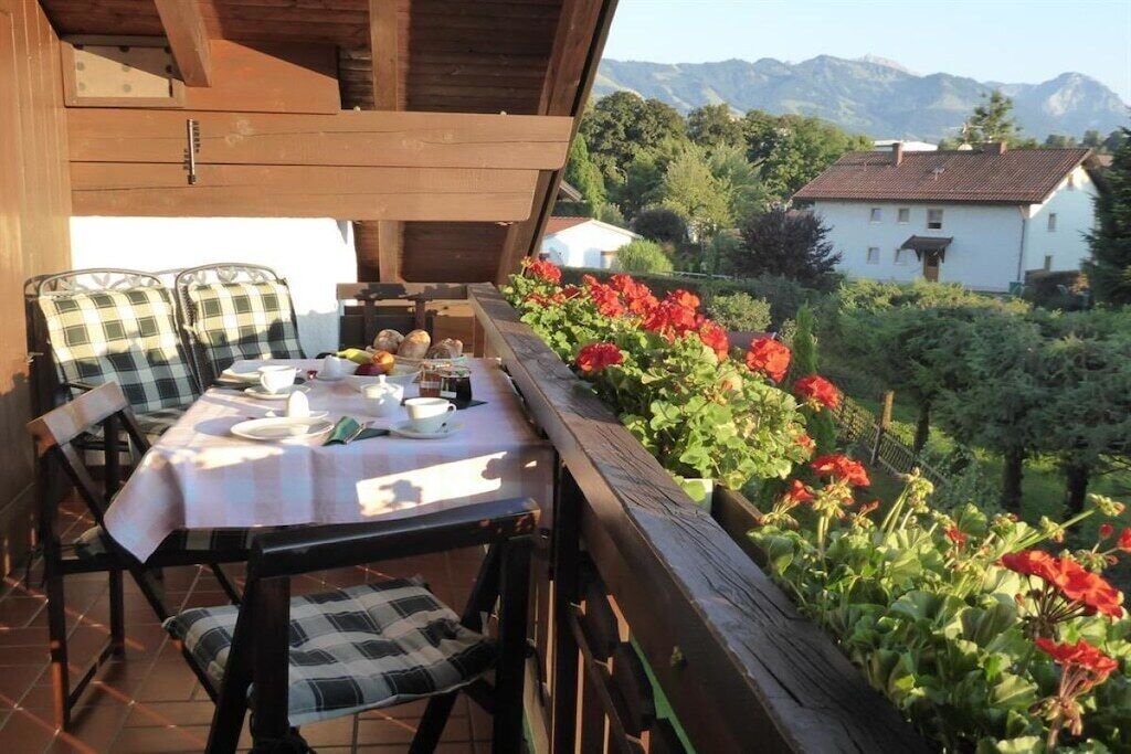 An outdoor dining area with a table set for two, surrounded by chairs with checkered cushions.
