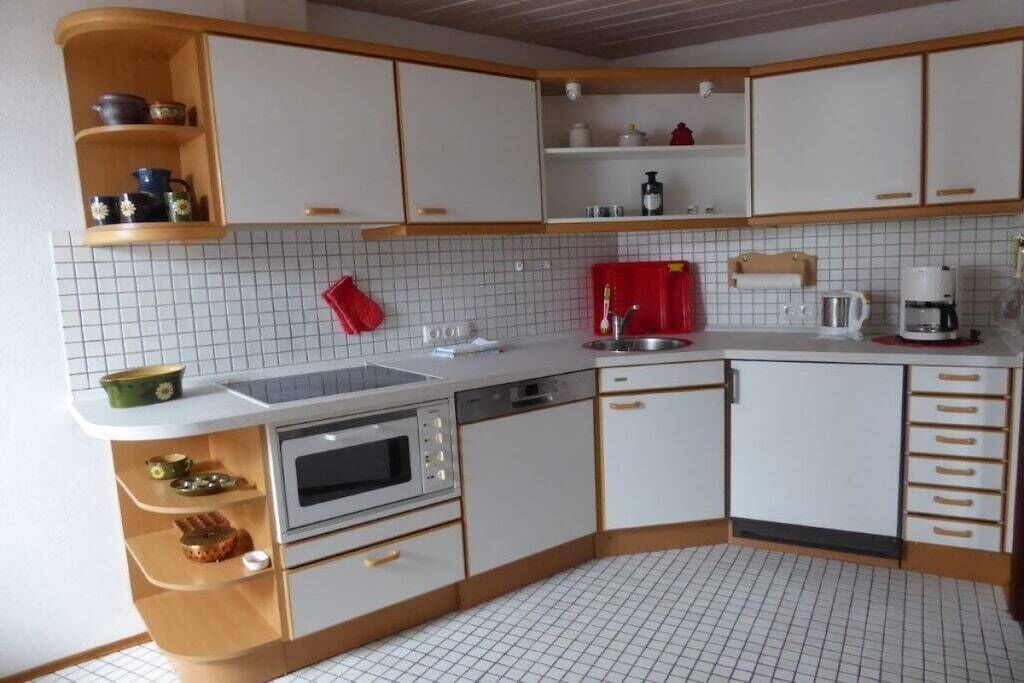 Eine kleine Küche mit weißen Schränken, einer Mikrowelle, einem Spülbecken und einer Kaffeemaschine.
