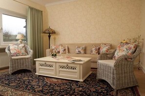 A living room with wicker furniture, a patterned rug, and a window with curtains. - Holiday apartment with 1 bedroom (Grünendeich)