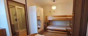 Ein kleiner, kompakter Raum mit Etagenbett, Duschbereich und Kleiderschrank.