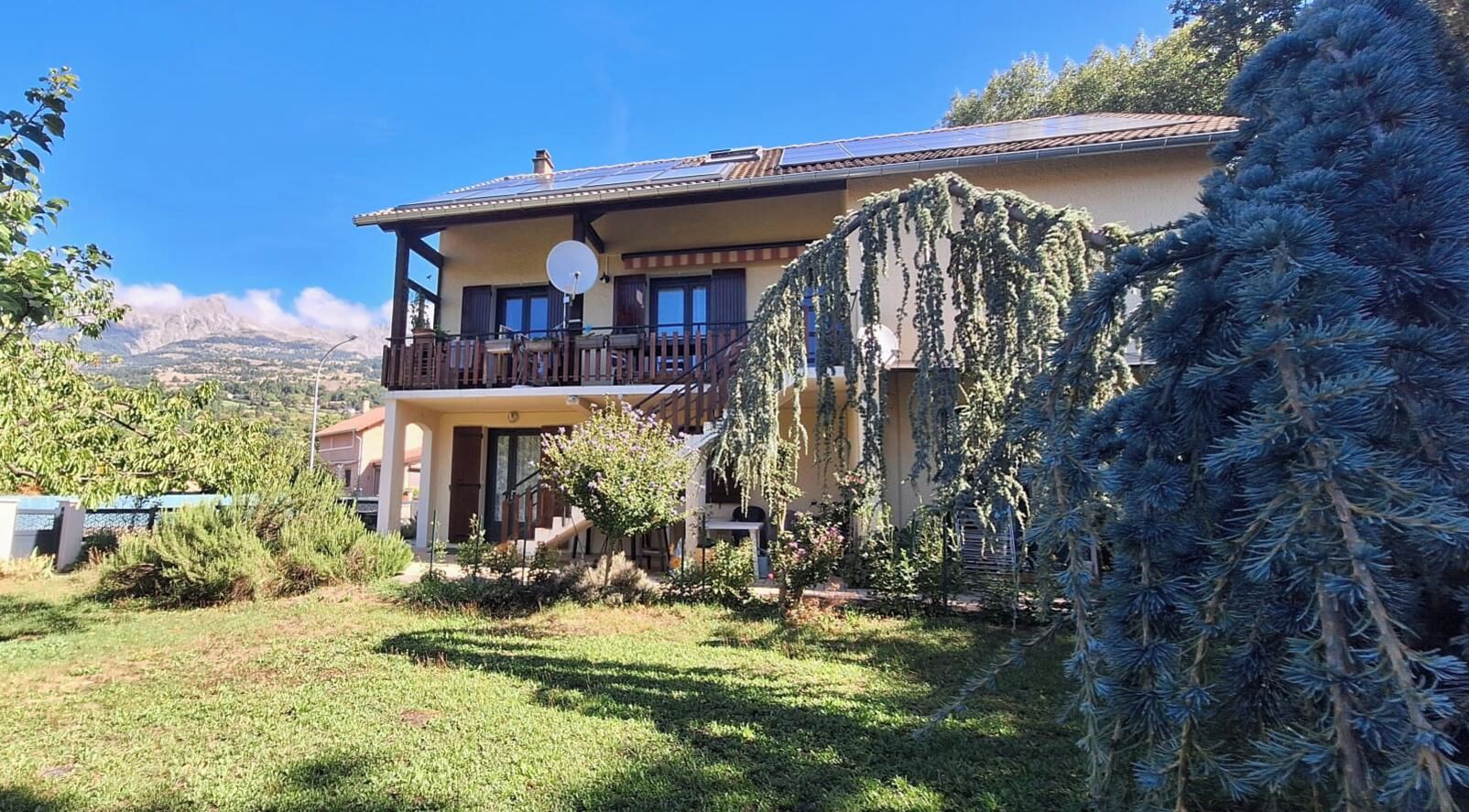 A two-story building with a balcony, surrounded by greenery and a mountainous backdrop.