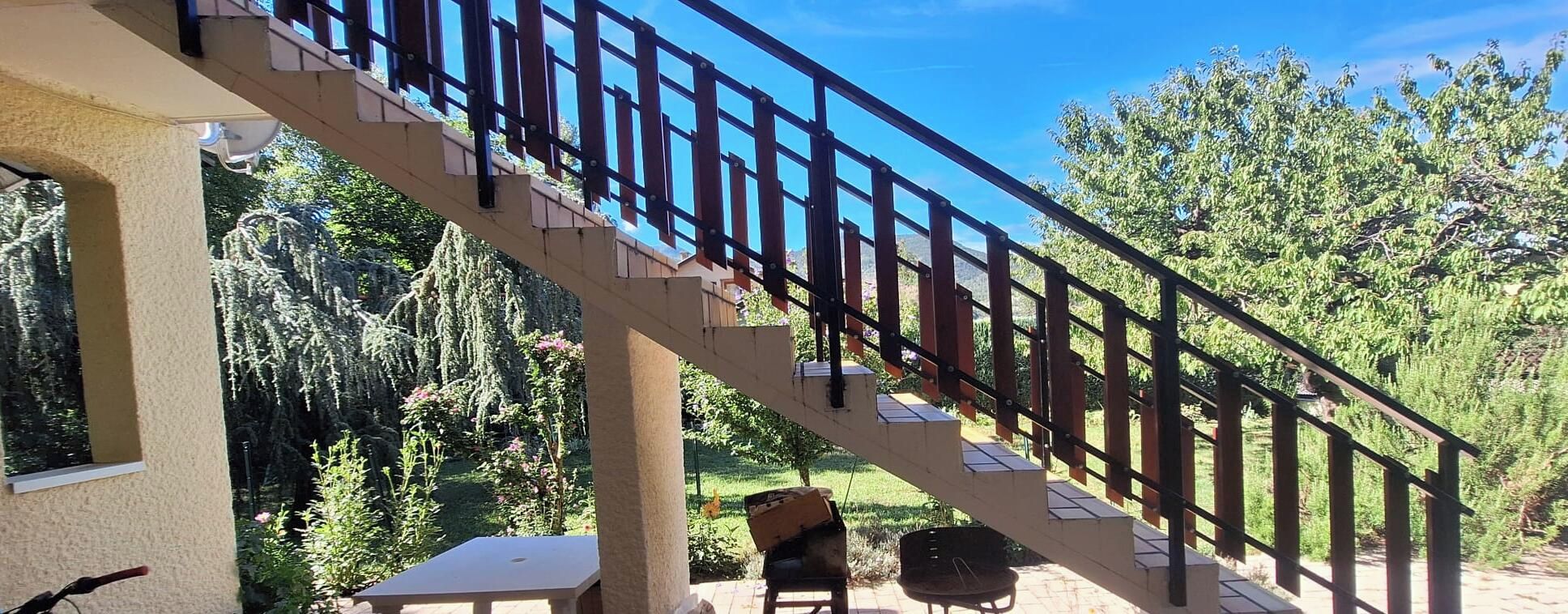Escadaria com corrimão metálico que leva a um nível superior, cercada por vegetação e árvores.