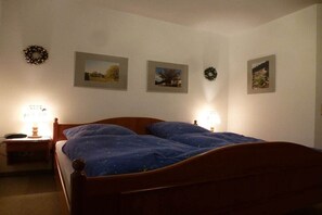 A bedroom with a wooden bed, two bedside lamps, and three framed pictures on the wall. - Holiday apartment with 2 bedrooms (Lenzkirch)