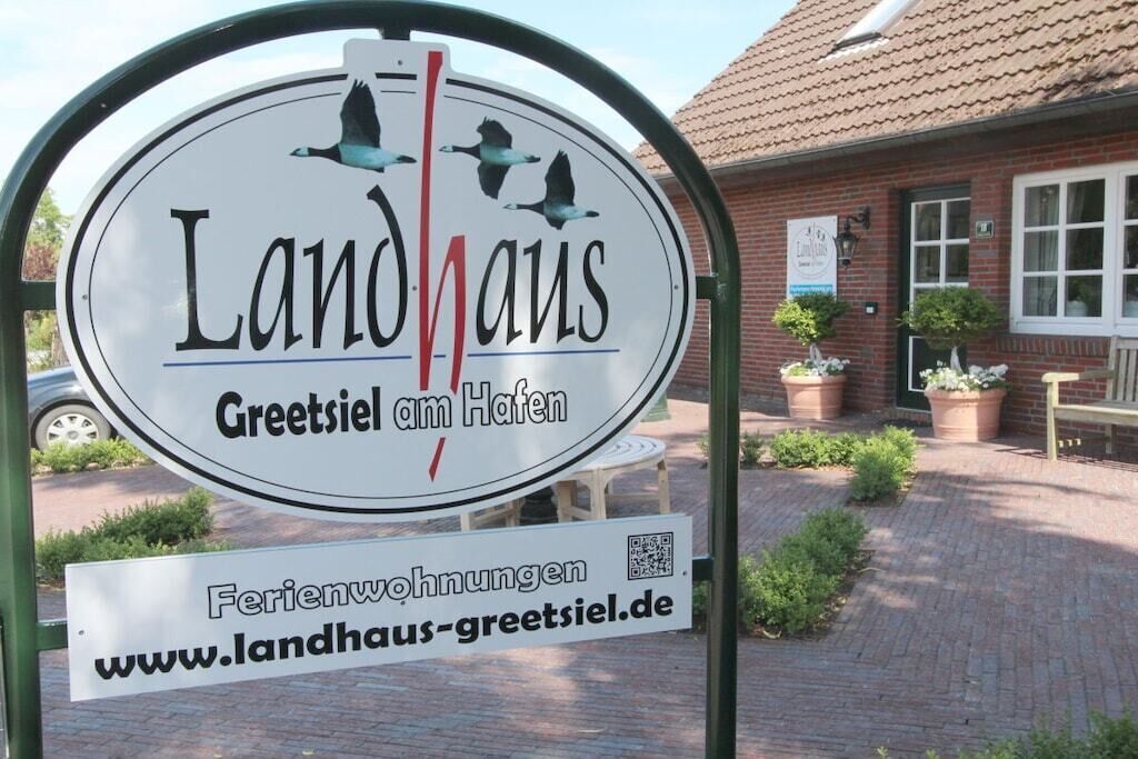 Un cartel que indica 'Landhaus Greetsiel am Hafen', con un código QR y una dirección web.