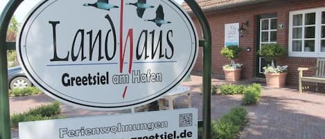 Un cartel que indica 'Landhaus Greetsiel am Hafen', con un código QR y una dirección web.