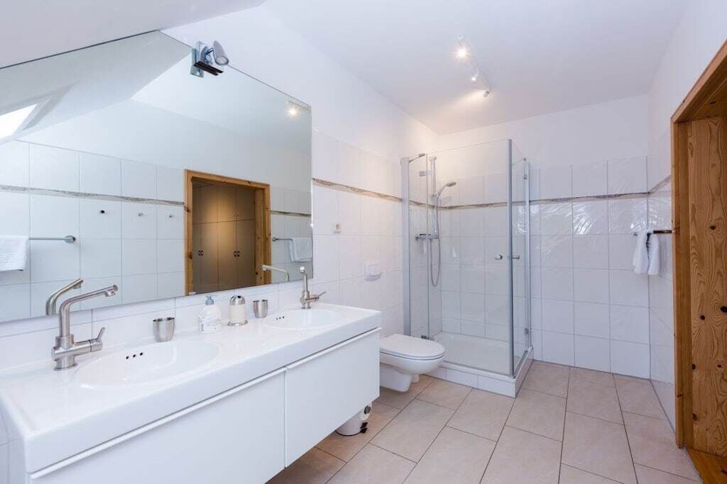 Un baño moderno con tocador doble, cabina de ducha de vidrio y puerta de madera.