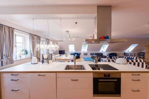 A modern kitchen with a central island, built-in oven, and a dining area with a view of the living room. - Holiday apartment with 2 bedrooms (Krummhörn-Greetsiel)