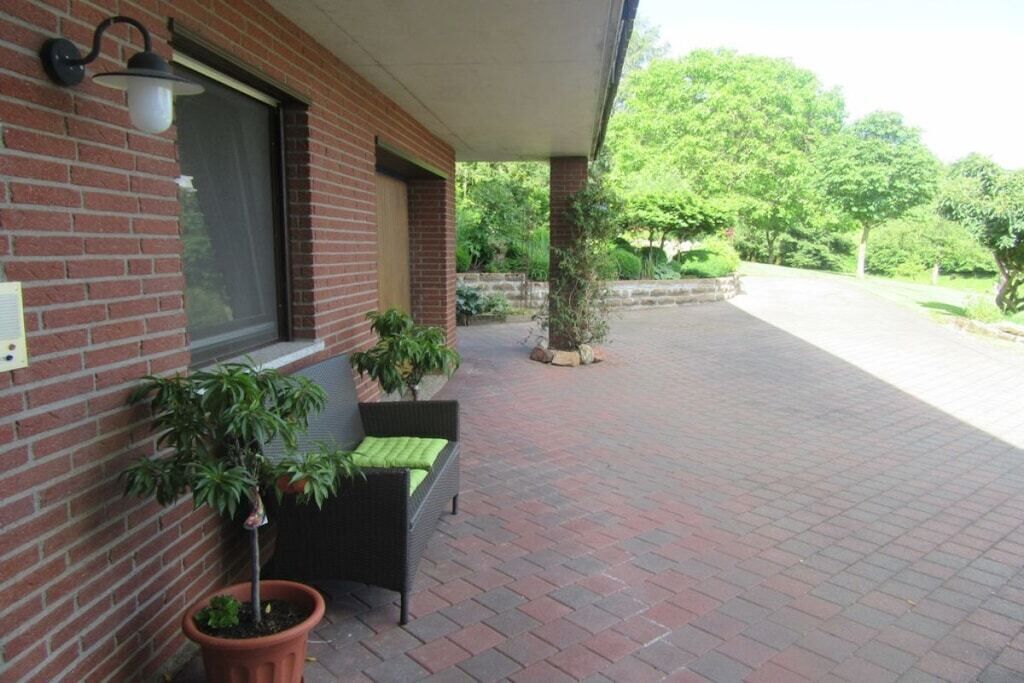 En murstensbygning med en overdækket terrasse, en potteplante og en fletstol.