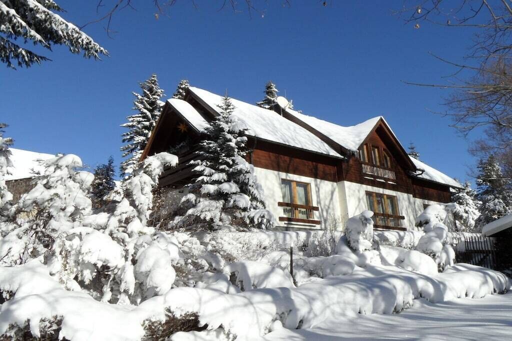 A wooden cabin with a snow-covered roof, surrounded by snow-laden trees.