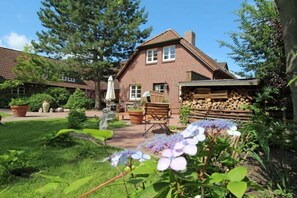 Une maison en briques avec un jardin, un espace extérieur aménagé pour s’asseoir et une pile de bois de chauffage.