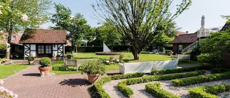 Un jardín con un camino pavimentado, setos cuidadosamente recortados y una variedad de plantas en macetas.