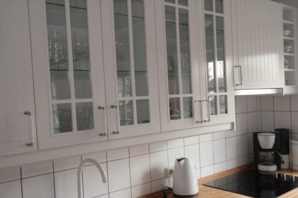 Une cuisine avec des meubles blancs, une plaque de cuisson noire et une machine à café.