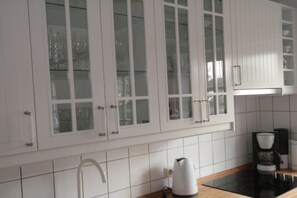 Une cuisine avec des meubles blancs, une plaque de cuisson noire et une machine à café.