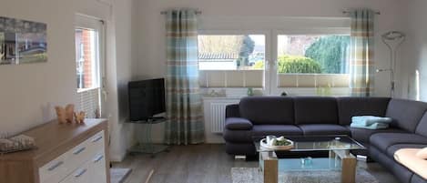 A living room with a sofa, a coffee table, a TV, and a window with curtains.