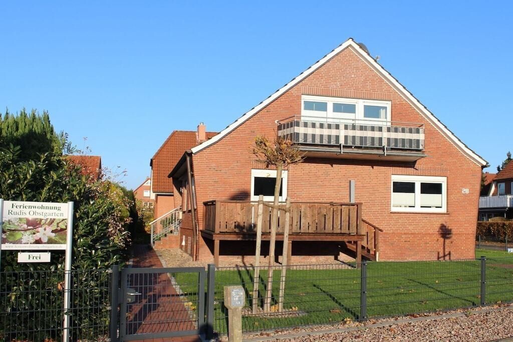 Une maison à deux étages, construite en briques, dotée d’un balcon, d’une terrasse en bois et d’un petit jardin.