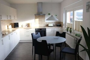 A modern kitchen with white cabinets, a round dining table, and black chairs. - Rudi's orchard "Este" (Jork)