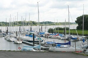 A marina with multiple boats docked, surrounded by greenery and a body of water. - Rudi's orchard "Este" (Jork)