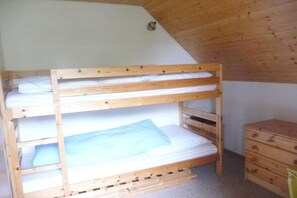 Ein Etagenbett mit drei Schlafstellen, eine Holzkommode und eine schräge Decke.