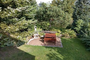 A garden with a wooden bench, a stone fireplace, and a variety of trees. - "East" in the holiday home "Keilbergblick" (Kurort Oberwiesenthal)
