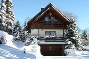 A log cabin with a balcony, surrounded by snow-covered trees. - "East" in the holiday home "Keilbergblick" (Kurort Oberwiesenthal)