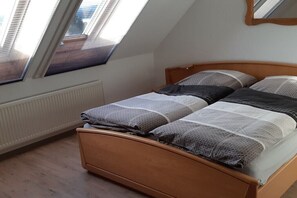 Ein Schlafzimmer mit schrägem Dach, einem Bettgestell aus Holz und einem Fenster mit Jalousien.