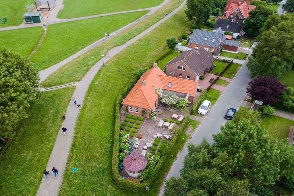 Vista aérea de una zona residencial con una casa de techo rojo, un jardín con un pabellón y un camino de entrada pavimentado.