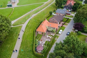 An aerial view of a residential area with a house featuring a red roof, a garden with a gazebo, and a paved driveway. - Holiday home with 2 bedrooms (Krummhörn)