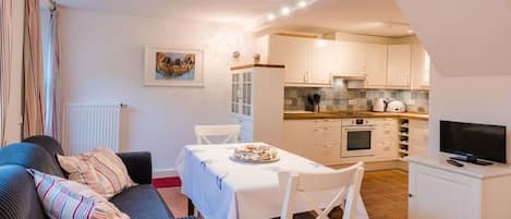 A compact living space with a dining area, kitchenette, and a television on a stand.