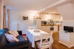A compact living space with a dining area, kitchenette, and a television on a stand. - Holiday home with 2 bedrooms (Krummhörn)