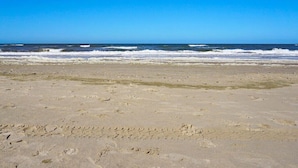 Ein Strand mit Fußspuren, die zum Wasser führen, ein klarer Himmel und der Ozean im Hintergrund.