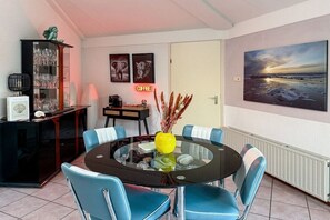 A dining area with a round glass table, blue chairs, a coffee station, and a painting on the wall. - Holiday home with 2 bedrooms (Julianadorp)