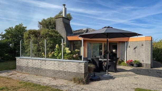 Ein modernes Haus mit einer Terrasse, Sitzgelegenheiten im Freien und einem Schornstein.