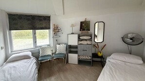 Ein Schlafzimmer mit zwei Betten, einem Fenster mit Blick, einem Nachttisch mit Lampe, einem Spiegel und einem Ventilator.