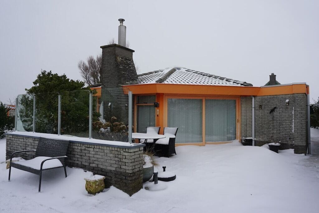 Een modern huis met een gevel van baksteen, een schoorsteen en een overdekt terras met tuinmeubels.