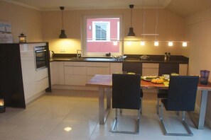 Une cuisine compacte comprenant une table à manger, des chaises et une fenêtre donnant sur un immeuble rouge.