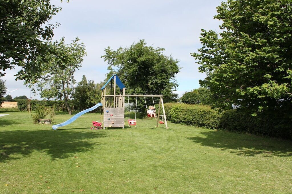 A playground with a slide and swings in a grassy area surrounded by trees.