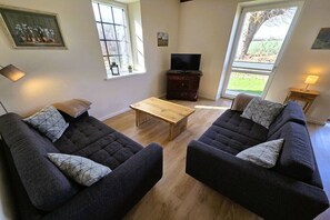 A living room with two dark sofas, a wooden coffee table, and a television on a stand. - Old Dairy Twedt - Boiler Room (Twedt)